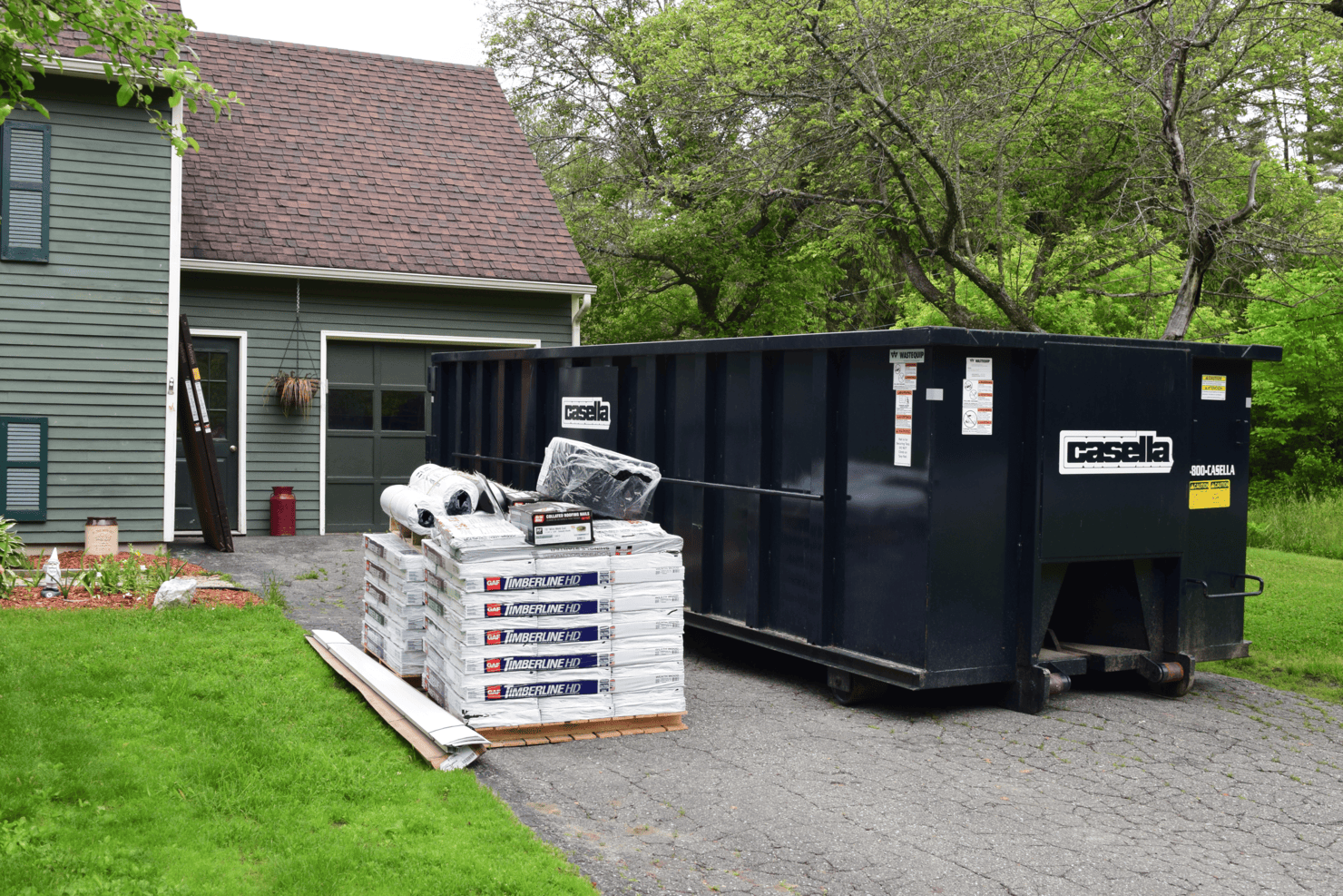 Casella roll-off dumpster sitting in home driveway aside stacks of material